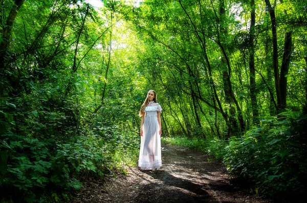 Girl in a long transparent white dress in the forest in the rays of the sun. Soft focus.
