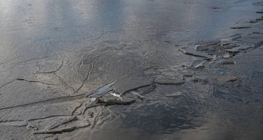 Bir bahar gölü üzerinde eriyen ince buzun dokusu ve yüzeye yansıyan gökyüzü. Işık parlaması.