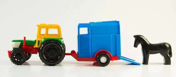 Plastic toy multi-colored tractor with a van for transporting horses on a white background.