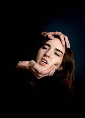 Erkeklerin elleri bir kadının kafasını siyah arka planda tutar. Korku, acı.