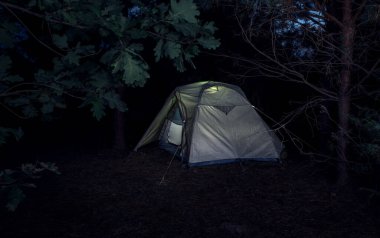 Akşam ormanında ağaçların arasında aydınlatılmış bir çadır..