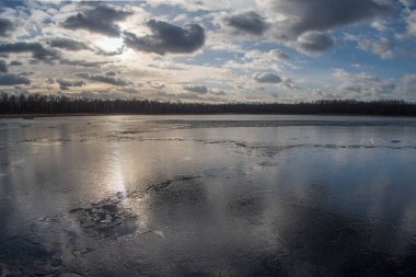 Spring lake covered with thin transparent cracking ice.