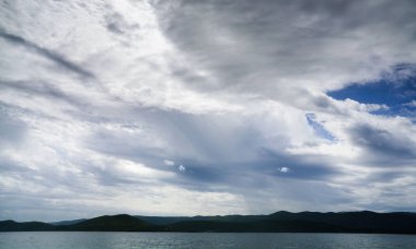 Denizin üzerindeki bulutlu gökyüzü ve dağların silueti.