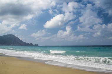 Dalgalar bulutlu gökyüzünün altında kumlu plajlara çarpıyor.