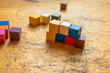 Eski ahşap bir yüzeye kısmen istiflenmiş küçük renkli tahta küplerden oluşan bir sıra.