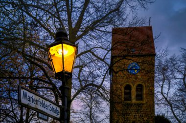 Arka planda tarihi bir köy kilisesi olan tarihi fener, Berlin 'de mavi saat..