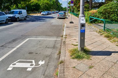 Berlin, Almanya - 11 Ağustos 2022: Bir fenerde elektrikli arabalar için halka açık bir şarj istasyonuna bakın. Odak ön plandaki simgeye uzanır.