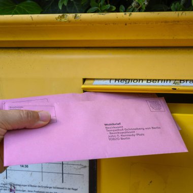 Berlin, Germany - June 2, 2024: A man's hand putting the documents for a postal vote in a mailbox. clipart