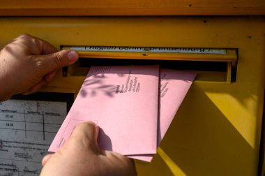 Berlin, Germany - June 2, 2024: A man's hand putting the documents for a postal vote in a mailbox. clipart