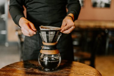Kahve makinesi ve su ısıtıcısının üzerine dökülen kimyasallarla kahve hazırlayan profesyonel barista.