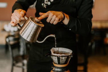 Kahve makinesi ve su ısıtıcısının üzerine dökülen kimyasallarla kahve hazırlayan profesyonel barista.