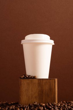 Kahverengi arka planda, kahve çekirdekleri ile plastik kapaklı, tek kullanımlık boş kağıt bardak.