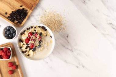 Sağlıklı yulaf ezmeli kahvaltı, böğürtlen, muz ve ahududu. Doğal malzemeler. Mermer arka planda düz dizayn.