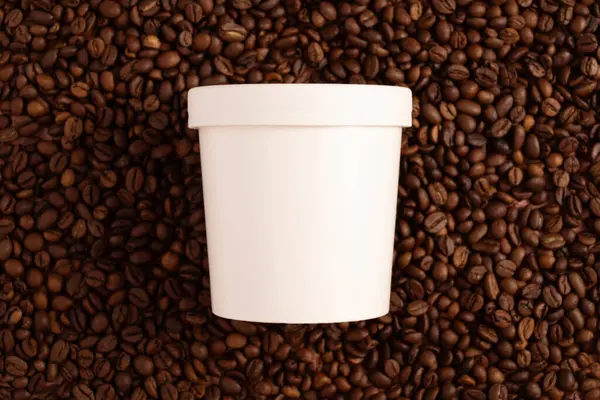 Blank disposable paper packaging with a lid mock-up on brown background with coffee beans