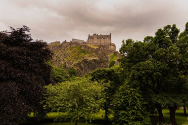 Photo of Edinburgh Castle between the foliage taken from the Princess Street garden during a cloudy summer day