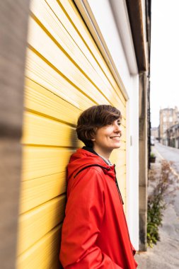 Portrait of an attractive young female wearing a red raincoat with a yellow door in the background