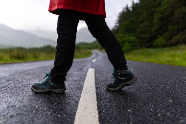 Detailed photo of a person's legs while crossing a road with fir trees in the background during a foggy day in the highlands, Scotland