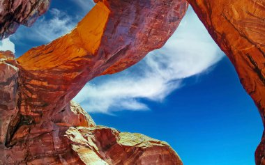Mavi gökyüzüne karşı kırmızı kumtaşı köprüsünün alçak açısı, yumuşacık yaz bulutları - Çifte Kemer, Arches Ulusal Parkı, Utah