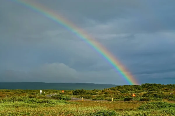 Lonely road through beautiful icelandic green rural  landscape after rain weather change with colorful rainbow - Iceland