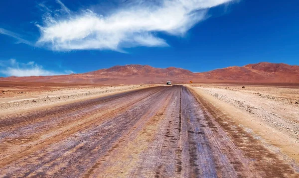 Straight empty sandy desert road through life hostile barren dry arid landscape, one single lone truck on horizon - Salar de Atacama, Chile