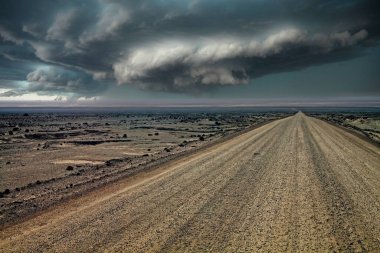 Monoton hayattaki sonsuz çakıllı yol çorak sürreal gri taş ve kum atacama çöl manzarası ufuktaki uğursuz kara yağmur bulutları