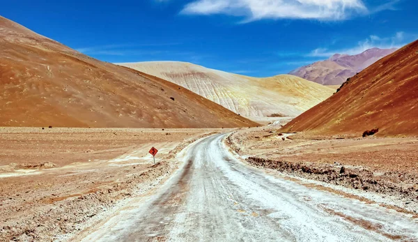 stock image Lonely empty sandy road in hilly dry bare lonely valley between colorful desert hills, something lost curves ahead sign   - Coridillera de Copiapo, Atacama, Chile