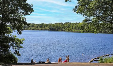 Leukermeer (Limburg), Hollanda - 9 Haziran. 2023: Güzel, cennet gibi bir Hollanda yüzme gölü, insanlar iskelede oturuyor, yeşil orman.