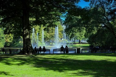 Breda, Hollanda - 30 Ağustos. 2023: Güneşli yaz gününde yeşil şehir parkındaki Valkenberg çeşmesinde, ağaçların gölgesinde, ağaçların gölgesinde tanınmayan insanlar oturuyor