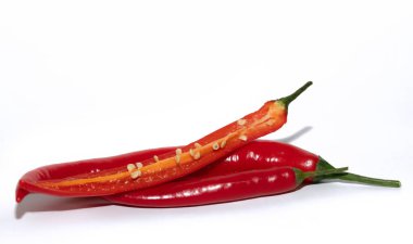 Taze ve kırmızı biberlerden yakın çekim. Bir meyve açık ve tohumları görebilirsiniz. Baharatlar beyaz bir arkaplan önünde birbirlerinin üstünde yatıyorlar.