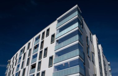 Münih 'te, Freiham bölgesinde yeni inşa edilmiş bir apartman var. Binanın birçok penceresi ve jöleli balkonları var. Arka planda mavi gökyüzü.