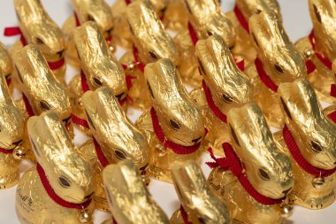 Lindt şirketinin çikolatasından yapılmış pek çok Paskalya tavşanı beyaz arka planda yan yana durur. Tavşanların kırmızı yakalı bir çanı var ve yan tarafından çekiliyorlar.