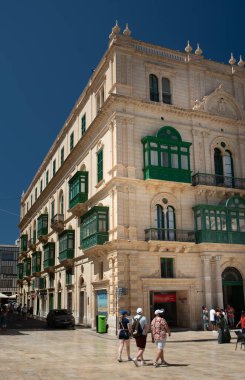 Bir grup turist Malta 'daki eski Valetta kasabasından geçiyor. Geleneksel balkonları olan tarihi bir binanın ön cephesinde..