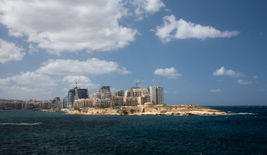 Malta 'da birçok gökdelen inşa ediliyor. Sahilde birçok yeni konut binası var. Vinçler arka planda. Arka planda mavi gökyüzü ve bulutlar, önplanda deniz..