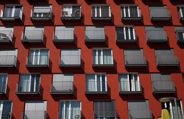 The brown-red facade of a residential building with many large windows and small balconies. The shutters are partially closed. It is a student residence.