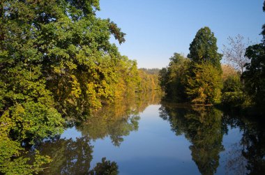 Ağaçların sonbaharda yavaşça sararması sakin bir nehre yansıyor. Gökyüzü mavi ve suya da yansıyor..
