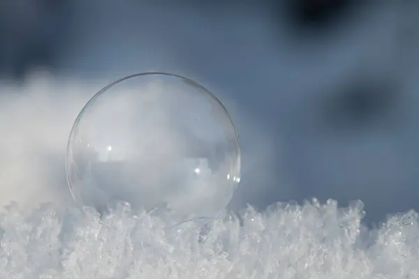 小さな透明な石鹸の泡は新鮮な雪の結晶の上にあります 背景はブルー テキストのためのスペースがあります ストック写真