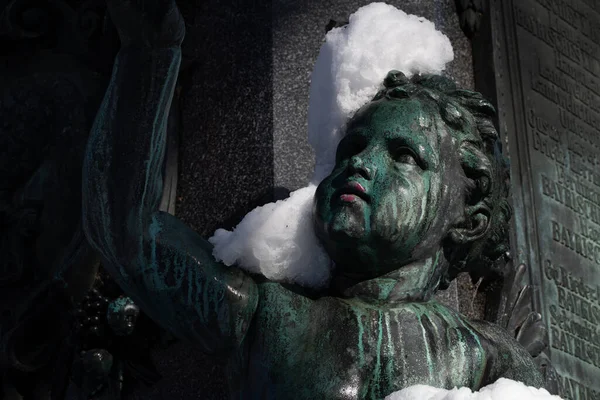 Close-up of a figure on a monument in the garden of the government of Swabia, Augsburg, Bavaria. Vandals have smeared the mouth of the child figure with red paint. There is snow on the bronze.