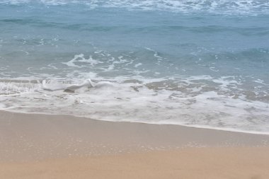 Dalgaların arka planı yavaşça sahile akıyor. Kumsalı, köpüklü dalgaları ve mavi denizi görebilirsiniz. Metin için boşluk var.