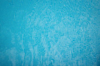 Yüzme havuzunun dibindeki arka plan ve doku küçük mavi fayanslarla kaplı. Su dipte küçük dalgalar oluşturuyor..