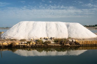 Mavi gökyüzüne karşı büyük bir deniz tuzu yığını. Tuz, tuz fabrikasının havzasına yansıyor..