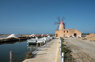 Bir patika Trapani yakınlarındaki bir yel değirmenine çıkıyor. Kenarda, gemiler kıyıya demir attı. Tuz fabrikasında tuz görülebilir..