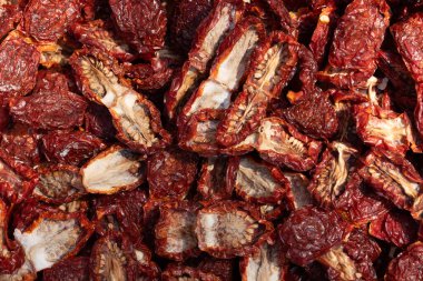 Kurutulmuş domatesler yan yana ve üst üste serilirler. Bazı domateslerin üzerinde hâlâ tuz var. Domatesler kesilmiş..