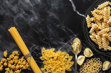 Farklı makarna türleri koyu bir arka planda mermer dokuya karşı yan yana yatar. Spiral şehriye, spagetti, tortellini ve diğer makarna çeşitlerini görebilirsiniz. Metin için boşluk var.