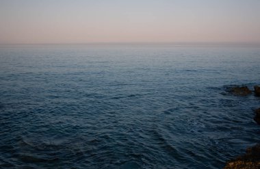 Denizde suyun arkaplanı, mavi dalgaları nazikçe yalayıp yutuyor. Arka planda, ufuk ve yumuşak ışık.