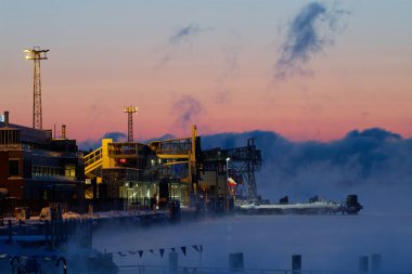 Helsinki, Finland - January 15, 2021: Docks and terminals of the Katajanokka Harbour on an extremely cold winter dawn with sea fog rising in the horizon. 