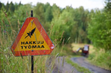 Nokia, Finland - July 31, 2023:  Woodworking site warning sign and forestry machinery on sunny July evening in Western Finland.  clipart