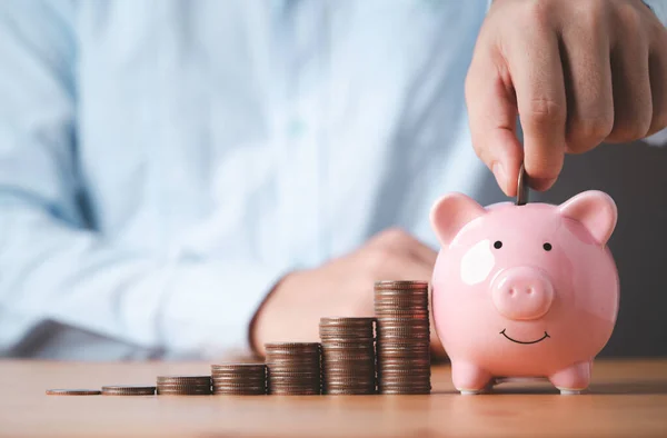 Businessman putting coin to pink piggy bank with increasing coins stacking on table , Money saving and deposit for investment to get profit and dividend concept.