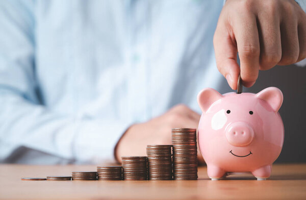 Businessman putting coin to pink piggy bank with increasing coins stacking on table , Money saving and deposit for investment to get profit and dividend concept. 