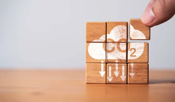 Hand assembly CO2 reducing icon on wooden block cube for decrease CO2 or carbon dioxide emission ,carbon footprint and carbon credit to limit global warming from climate change concept.