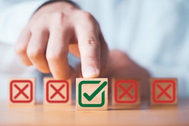 İşadamı, iş projesi önerisini onaylamak ve reddetmek için tahta blok üzerindeki Kızıl Haç işaretinin üzerine yeşil işaret işareti koyuyor.